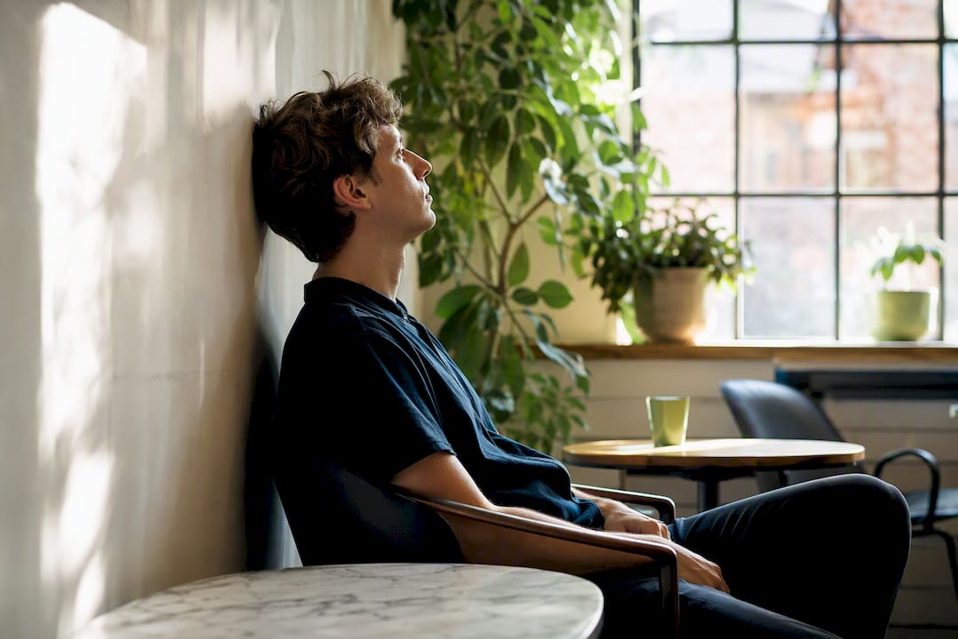 Young adult reflecting by window, subtle hypomania mood