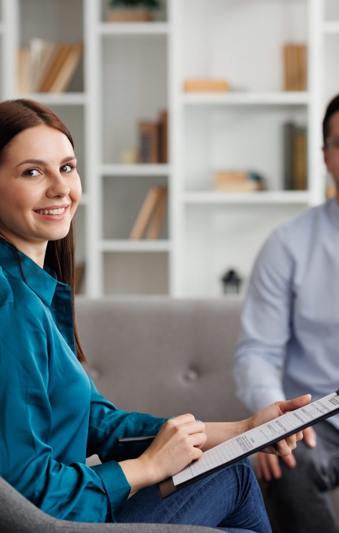 Portrait of professional psychologist consults a male patient in a state of stress and depression, who is sitting on sofa in the office. She writes on paper. The concept of a consultant psychologist